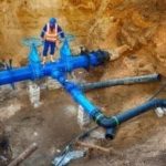 Worker in safety gear at a site installing blue and black water pipes for Chris Wilson Plumbing & Heating Repairs.