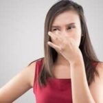 Woman in a red top holding her nose, portraying a reaction to unpleasant situations related to plumbing and HVAC services.