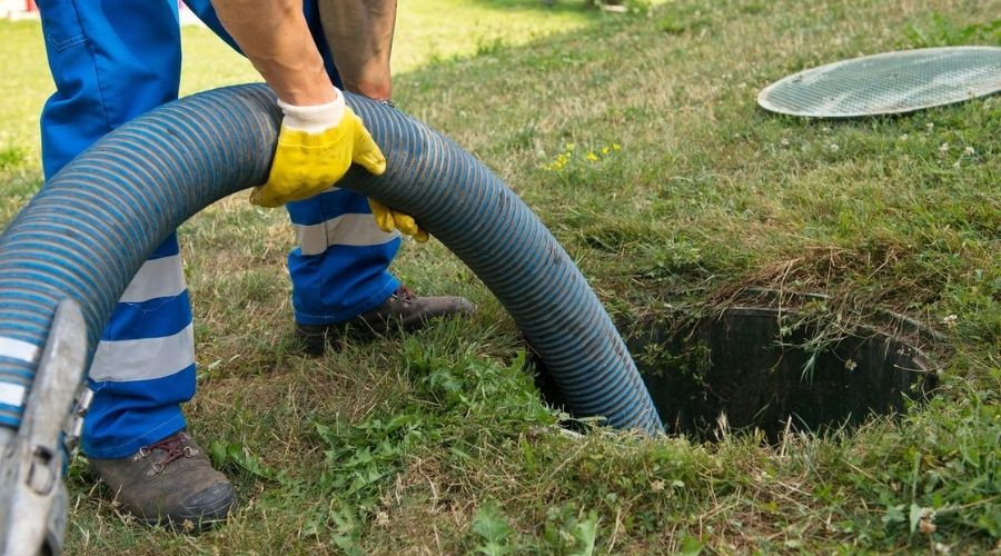 Plumber using a vacuum hose to clear outdoor pipe blockage in grassy area, emphasizing plumbing services by Chris Wilson Plumbing & Heating Repairs Inc.