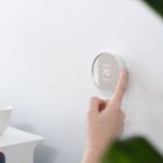 Person adjusting a smart thermostat on a white wall, emphasizing AC maintenance and energy efficiency.